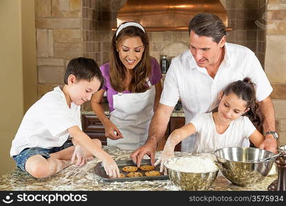 An attractive smiling family of mother, father, and two children baking and eating fresh chocolate chip cookies in a kitchen at home