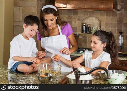 An attractive smiling family of mother, two children, girl, boy, son & daughter, breaking eggs & baking in a kitchen at home