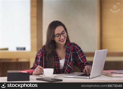 An attractive young businesswoman having coffee while working at her office desk