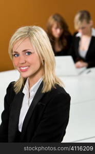 An attractive young female executive in focus in the foreground while her colleagues work on a laptop behind her