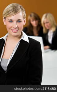 An attractive young female executive in focus in the foreground while her colleagues work on a laptop behind her