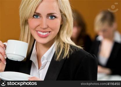 An attractive young female executive takes a coffee break while her colleagues work on a laptop behind her