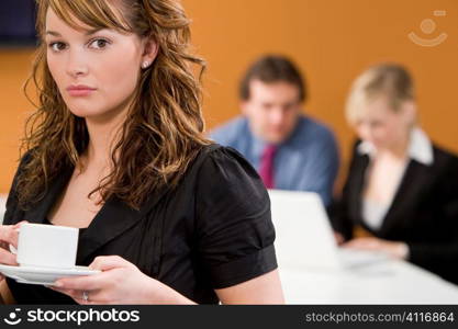 An attractive young female executive takes a coffee break while her colleagues work on a laptop behind her