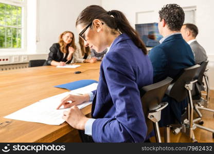 An attractive young woman is checking papers during a business meeting in a conference room - mixed caucasian team rather casual, ambiente might suggest a startup or an agency