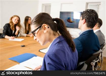 An attractive young woman is checking papers during a business meeting in a conference room - mixed caucasian team rather casual, ambiente might suggest a startup or an agency