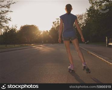 An attractive young woman is roller skating in a park at sunset
