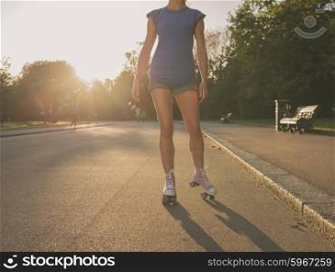 An attractive young woman is roller skating in a park at sunset
