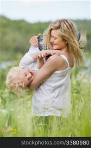 An attractive young woman playing with sweet little boy in green meadow