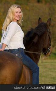 An attractive young woman riding a horse bareback during the fall