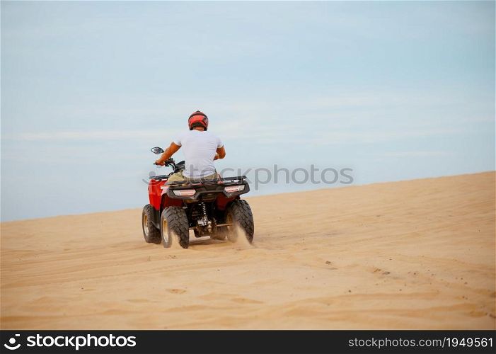 An atv rider racing in desert, downhill riding in desert sands, action view. Male person on quad bike, sandy race, dune safari in hot sunny day, 4x4 extreme adventure, quad-biking. An atv rider racing in desert