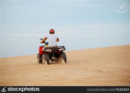 An atv rider racing in desert, downhill riding in desert sands, action view. Male person on quad bike, sandy race, dune safari in hot sunny day, 4x4 extreme adventure, quad-biking. An atv rider racing in desert