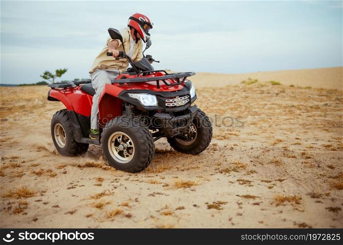 An atv rider racing in desert, downhill riding in desert sands, action view. Male person on quad bike, sandy race, dune safari in hot sunny day, 4x4 extreme adventure, quad-biking concept. An atv rider racing in desert