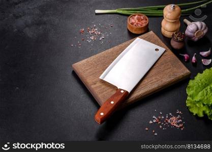 An axe for meat, spices and herbs, a cutting board against a dark concrete background. Cooking at home. An axe for meat, spices and herbs, a cutting board against a dark concrete background