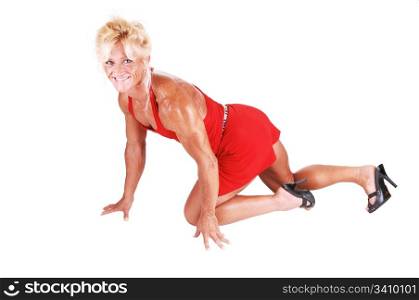 An blond bodybuilding girl kneeling on the floor of a studio and shooingher very muscular body with high heels and red dress, over white.