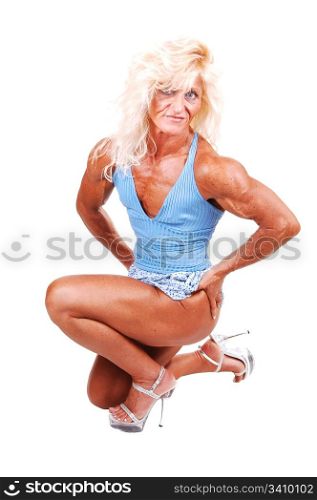 An blond bodybuilding girl kneeling on the floor of a studio and shooingher very muscular body with high heels and blouse top and shorts, over white.