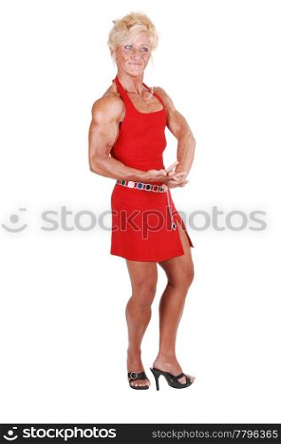 An blond bodybuilding girl standing in a studio in a red dress and shooingher very muscular body with high heels, over white background.