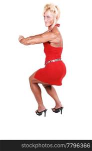 An blond bodybuilding girl standing in a studio in a red dress and shooingher very muscular body with high heels, over white background.