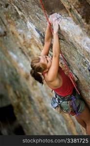 An eager female climber on a steep rock face looks for the next hold - viewed from above. Shallow depth of field is used to isolated the climber with the focus on the head.