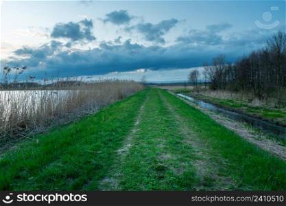 An earth embankment with a path by the Uherka river and the lake, Stankow, Lubelskie, Poland