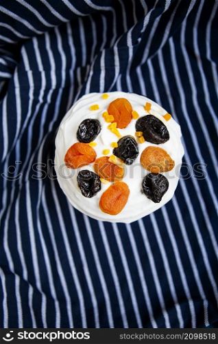 An Easter cake decorated with dried apricots and prunes stands on a blue striped apron. Easter religious holiday concept, top view. An Easter cake decorated with dried apricots and prunes stands on a blue striped apron. Easter religious holiday concept, top view.