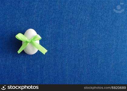 An easter egg with a green bow isolated on a blue background