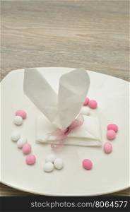 An Easter place setting with the napkin in the shape of bunny ears displayed in a plate with pastel color candy