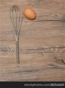 An egg beater, whisk, with one egg isolated on a wooden background