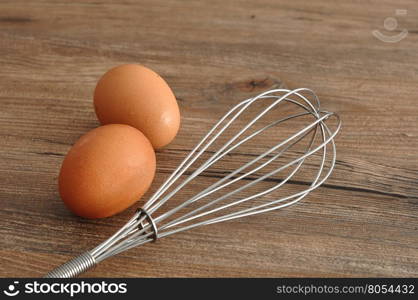 An egg beater, whisk, with two eggs isolated on a wooden background