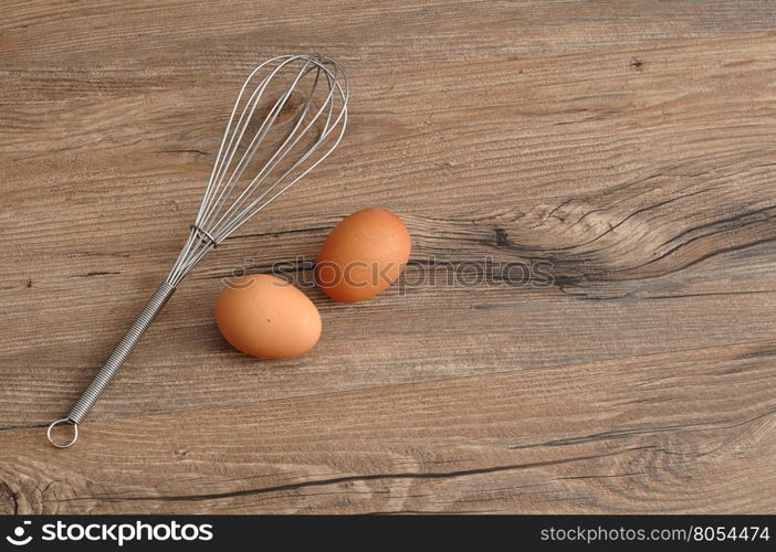 An egg beater, whisk, with two eggs isolated on a wooden background