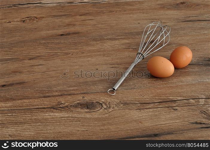 An egg beater, whisk, with two eggs isolated on a wooden background