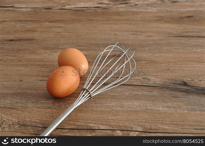 An egg beater, whisk, with two eggs isolated on a wooden background