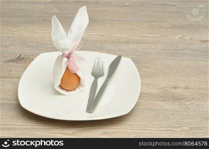 An egg in a napkin with bunny ears displayed on a plate with a knife and fork for Easter