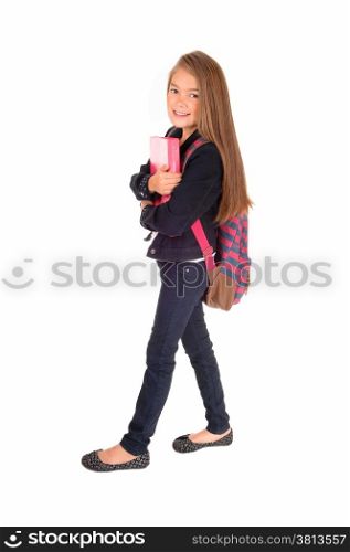 An eight year schoolgirl with her backpack over her shoulder standing forwhite background, holding her book.