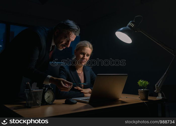 An elderly business man is advising company employees at the office during overtime , Two businessmen are discussing and solving work problems at the office at night.