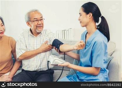 An elderly man having a blood pressure check by his personal caregiver with his wife sitting next to him in their home.. An elderly man having a blood pressure check by his personal caregiver
