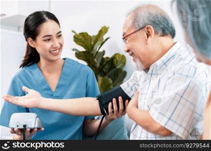 An elderly man having a blood pressure check by his personal caregiver with his wife sitting next to him in their home.. An elderly man having a blood pressure check by his personal caregiver