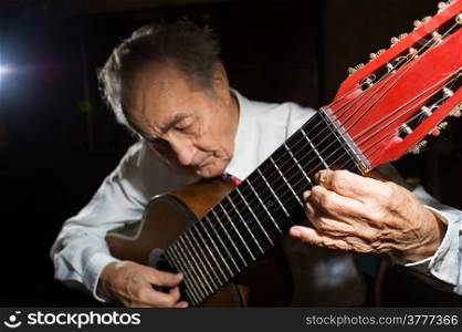 An elderly man in white shirt playing an acoustic guitar. Dark background. Focus on the hand.