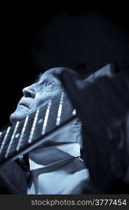 An elderly man in white shirt playing an acoustic guitar. Dark background. Monochrome.