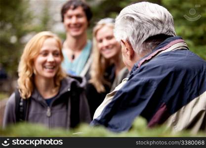 An elderly man talking to a group of young people in the forest.