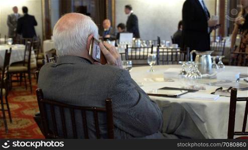 An elderly man uses phone in a dining room