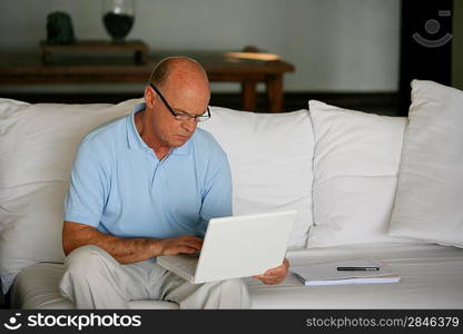 An elderly man working on his laptop at home