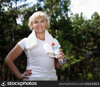 An elderly woman after exercising in the forest holding a bottle of water