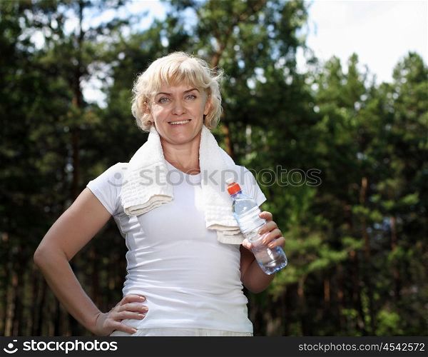 An elderly woman after exercising in the forest holding a bottle of water