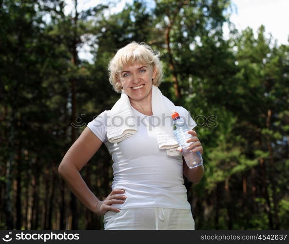 An elderly woman after exercising in the forest holding a bottle of water