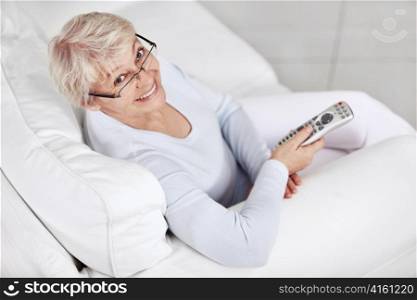 An elderly woman on the couch with remote control on TV