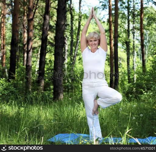 An elderly woman practices yoga in nature. The symbol of healthy lifestyle