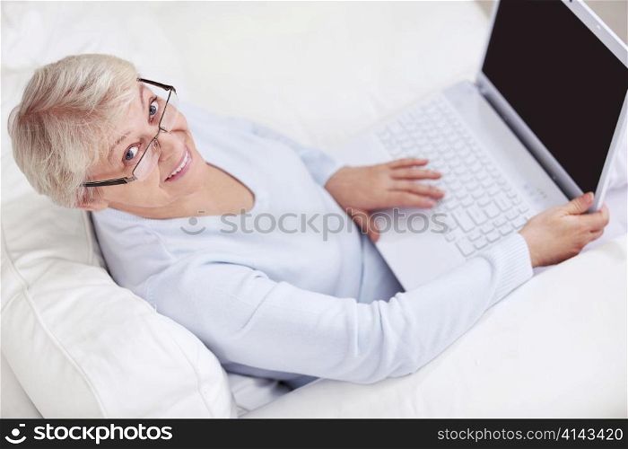 An elderly woman with a laptop on a white sofa