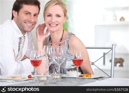 An elegant couple having dinner and smiling at us.