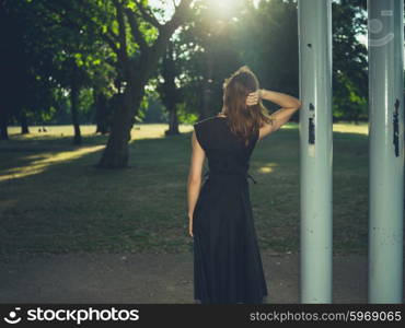 An elegant woman wearing a dress is standing under a bandstand at sunset