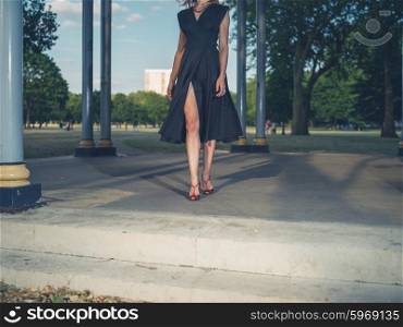 An elegant woman wearing a sexy dress is standing in a bandstand in a park at sunset